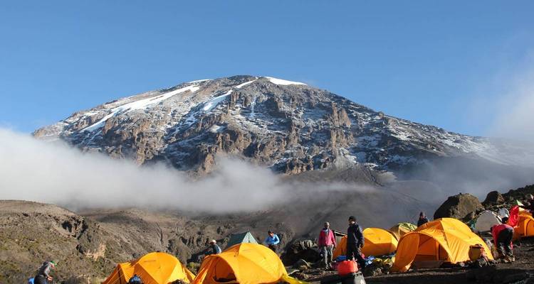 Terrain de camping avec des tentes orange vif et des personnes au pied d'une montagne enneigée.