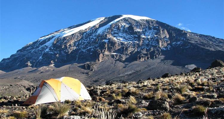 Une tente isolée dans un paysage rocheux au pied d'une montagne enneigée.