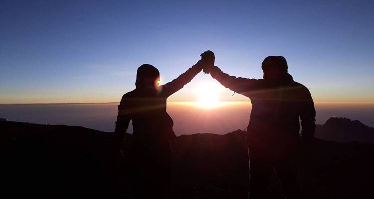 Silhouettes de deux personnes levant les bras en signe de victoire au lever du soleil.