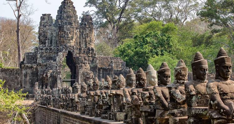 Stone gate of Angkor Thom flanked by a long row of guardian statues stretching into the jungle.