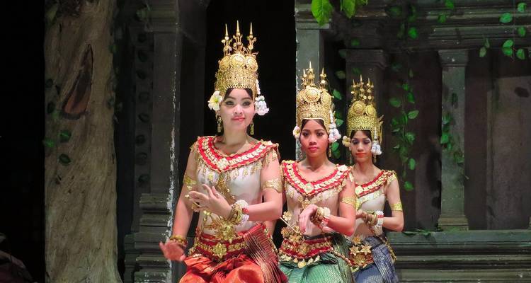 Three traditional Apsara dancers in ornate golden headdresses performing on stage.