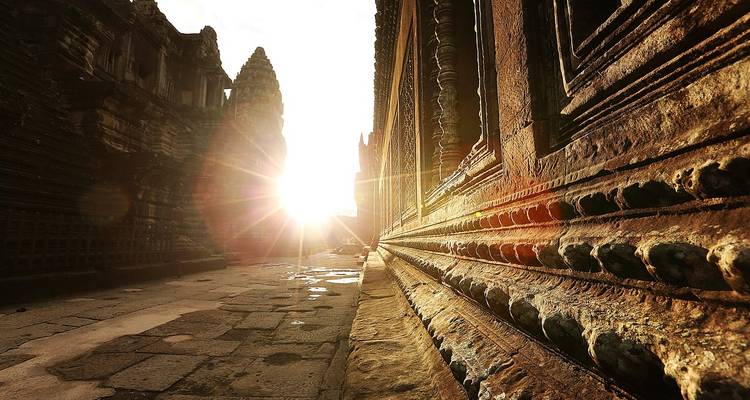Low-angle view of Angkor Wat corridor with dramatic sunburst shining through ancient stone towers.