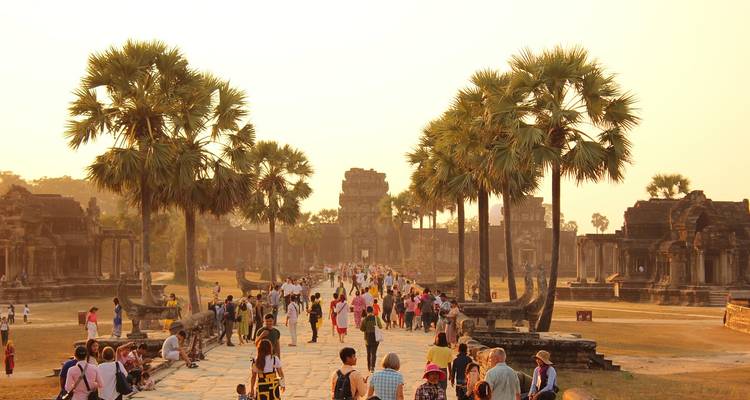 Busy sandstone causeway lined with palms leading to Angkor Wat packed with visitors during warm golden light.