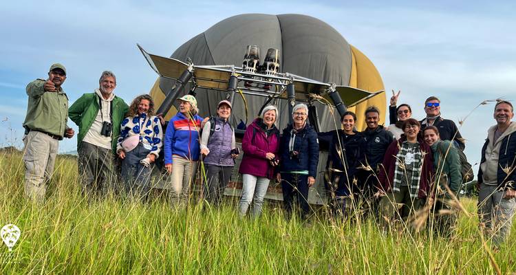 Group of people posing in front of a hot air balloon in a grassy field.