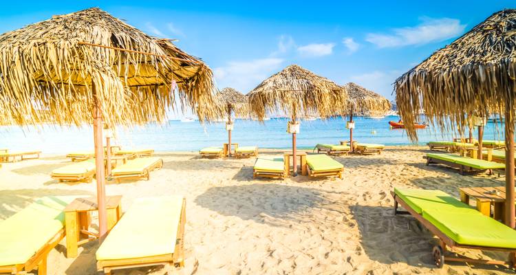 Plage ensoleillée avec parasols en paille et transats.