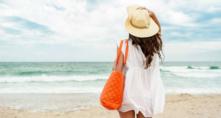 Personne face à l'océan sur une plage avec un sac orange sous un ciel nuageux.