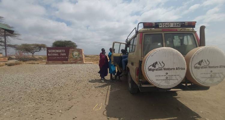 Véhicule de safari et panneau du parc national du Serengeti avec des personnes à proximité.