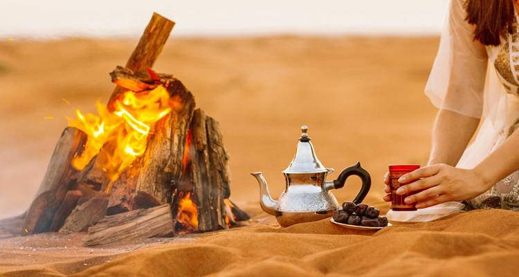 Installation de feu de camp confortable dans le désert avec thé et dattes.