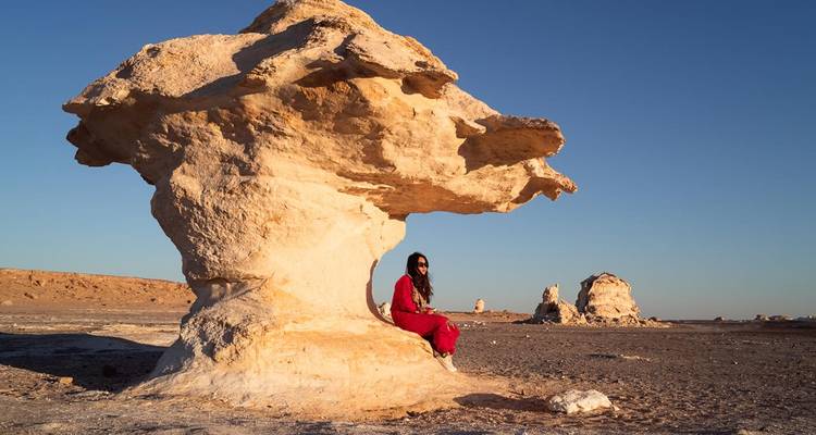 Personne assise sous une grande formation rocheuse dans un paysage désertique.