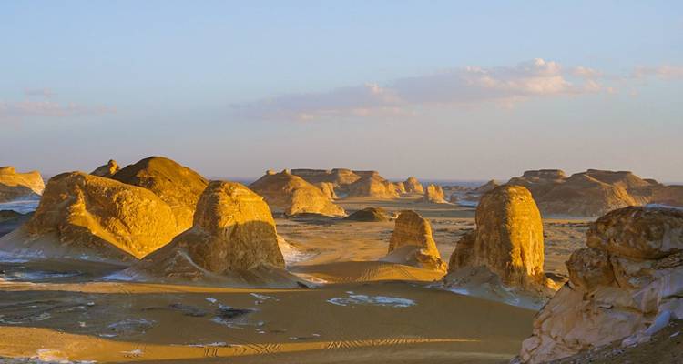 Désert avec des formations rocheuses éclairées par le soleil couchant.