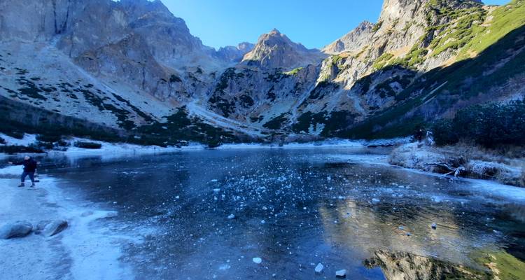 Frozen lake surrounded by snowy mountains with a person approaching.