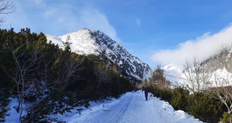 Snowy mountain path with two people walking towards a peak.