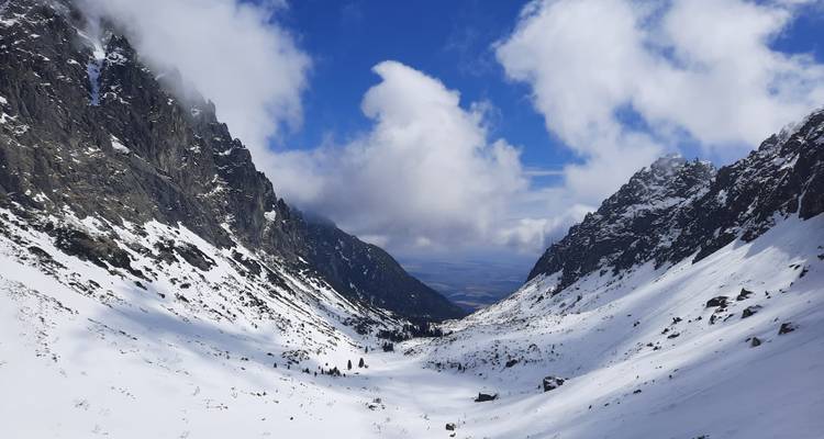 Snow-covered valley between two jagged peaks under a blue sky.