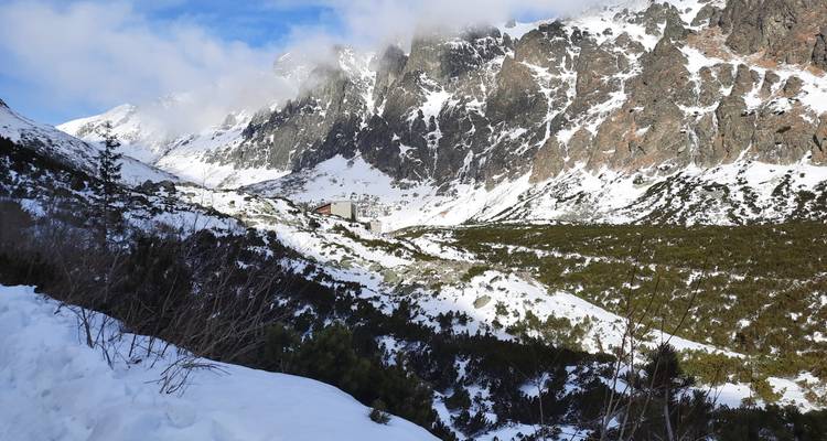Mountain landscape with snow patches and a distant lodge.