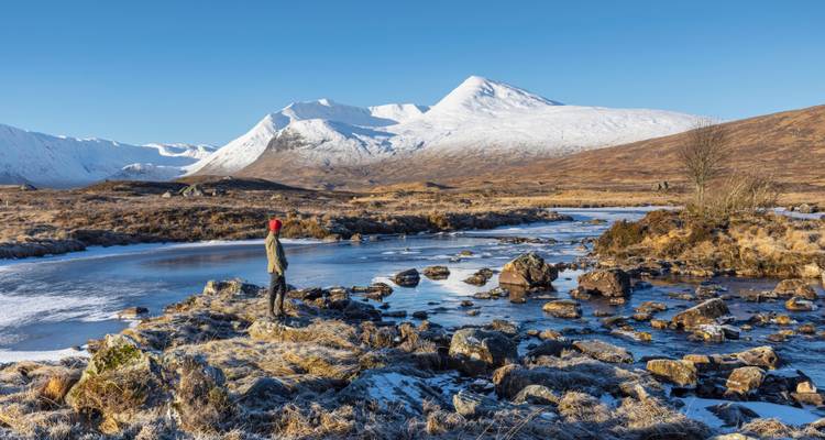 Montagnes enneigées vues à travers une rivière partiellement gelée.