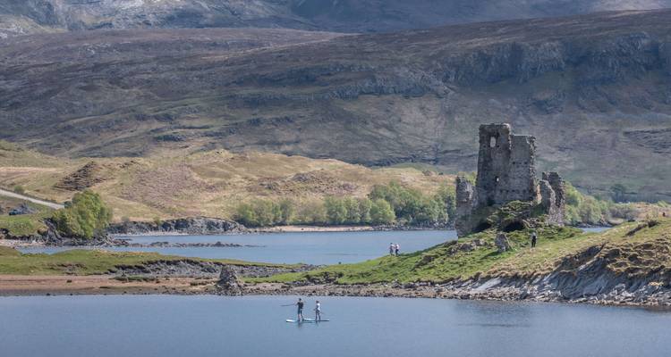 Deux pratiquants de paddle devant des ruines antiques au bord d'un lac.