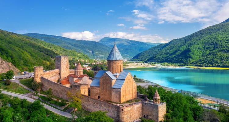 Historisch klooster aan een blauw meer omringd door bergen.