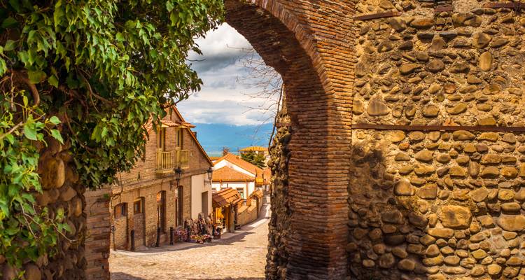 Uitzicht op kasseienstraat door een boog met bergachtergrond.