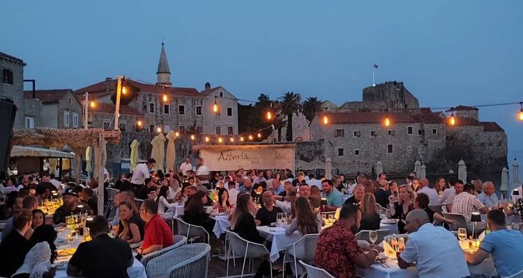 Scène de dîner en plein air le soir avec beaucoup de monde et des guirlandes lumineuses.