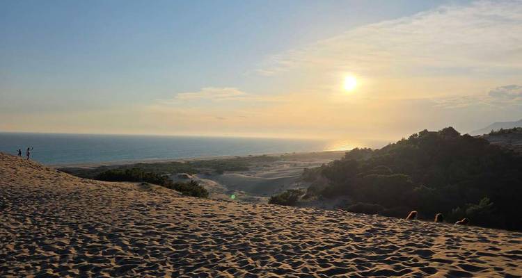 Gouden zon die ondergaat boven uitgestrekte kustduinen die een kalme zeehorizon ontmoeten.
