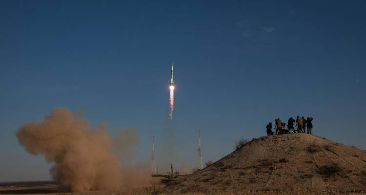 Raketenstart in den Himmel mit Zuschauern in der Ferne.
