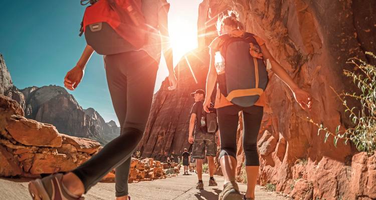 Des gens qui font de la randonnée sur un sentier de canyon ensoleillé.