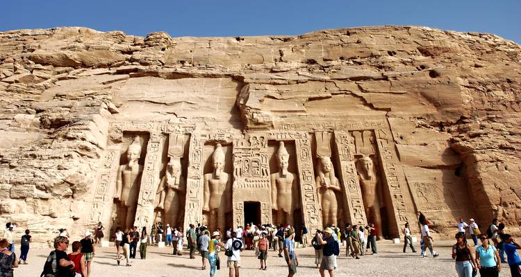 Los turistas exploran la fachada del templo excavado en roca de Abu Simbel bajo un sol radiante.