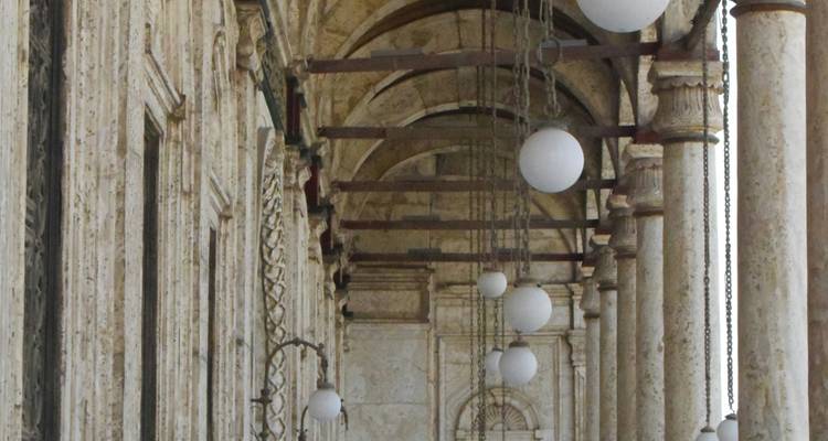 Arches et colonnes ornementales avec des lampes sphériques suspendues dans un bâtiment historique.