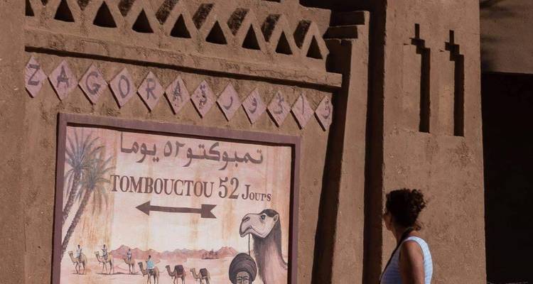 Person standing by a wall with a sign pointing to Timbuktu.