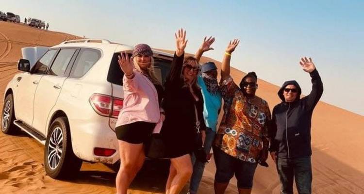 Group of people posing in the desert by a vehicle.