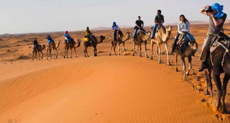 Camel caravan with people riding through the desert.