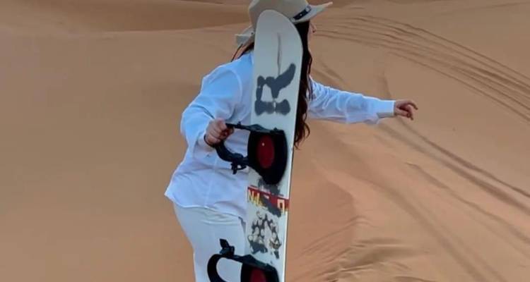 Person sandboarding on a desert dune.