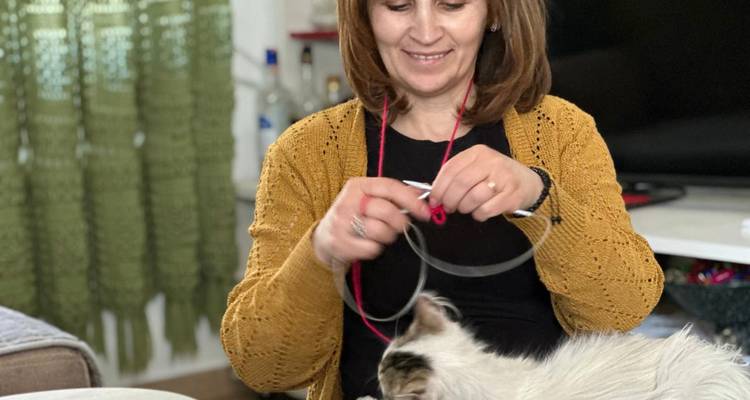 Personne qui tricote avec un chat assis à côté d'elle.