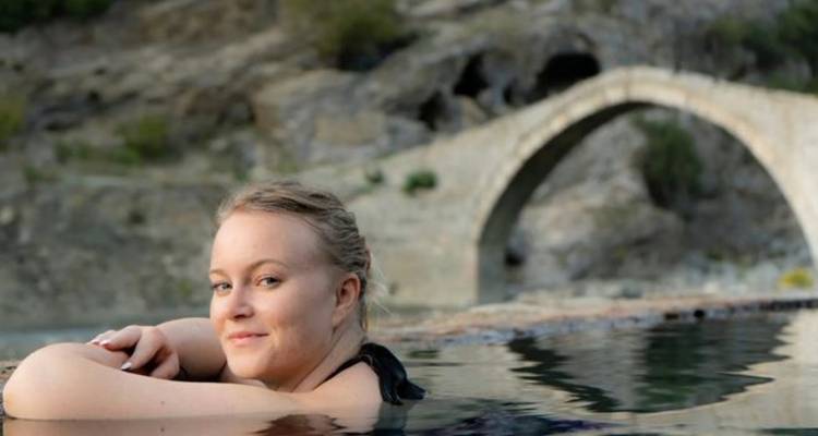 Personne flottant dans une piscine avec un pont de pierre en arrière-plan.