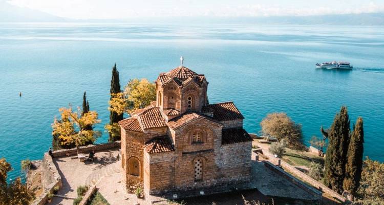 Église ancienne au bord d'un lac avec un bateau qui passe.