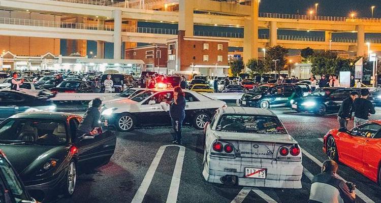 Groep auto's en mensen in een drukke straatscène 's nachts.