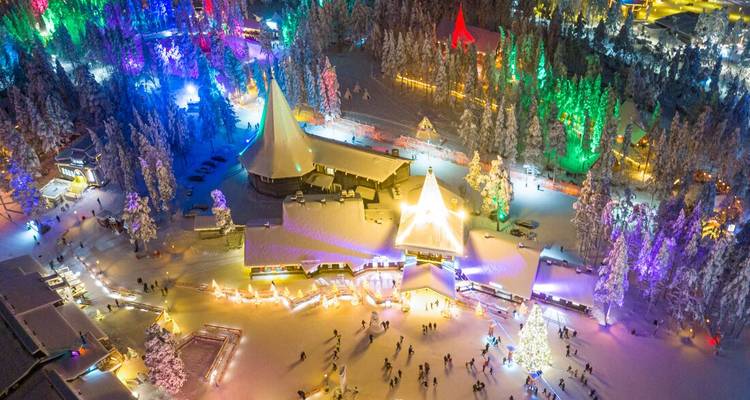 A snowy village illuminated by colorful lights at night.