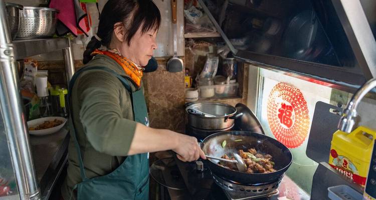 Una mujer cocinando en una cocina pequeña con ingredientes vibrantes a su alrededor.