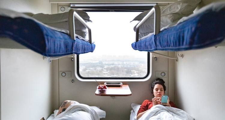 Two people resting in a train compartment with bunk beds.