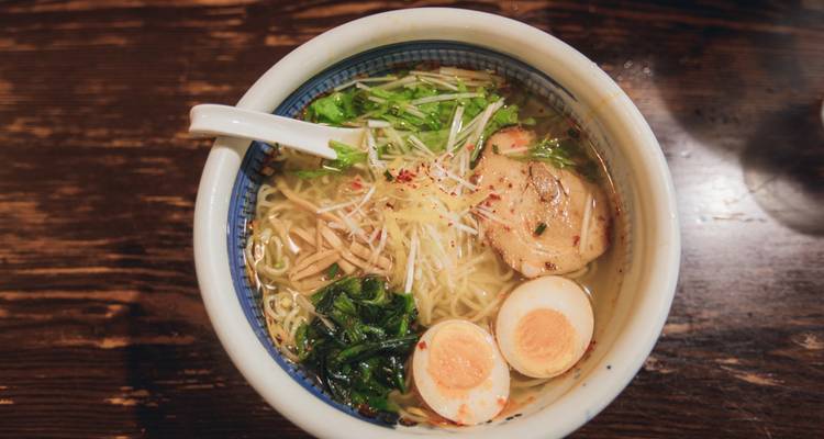 Bowl of ramen with eggs and greens on a wooden table.