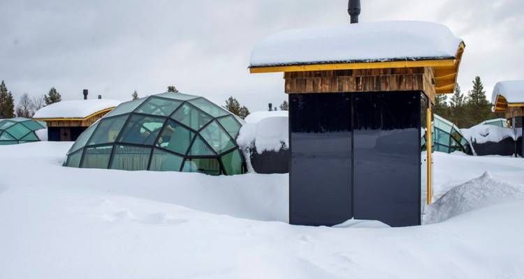 Glass domed igloos resting on thick snow under a cloudy sky.
