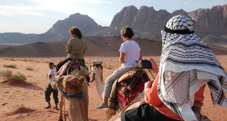 Des personnes montant des chameaux dans une zone désertique avec des montagnes en arrière-plan.