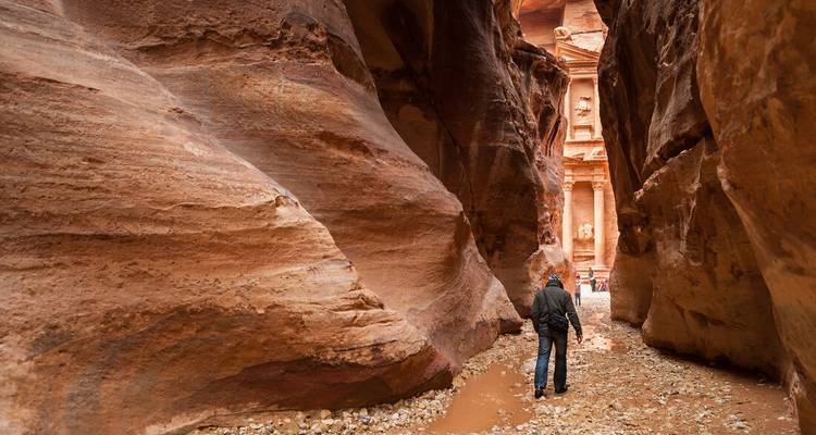 Une personne marchant à travers un passage rocheux étroit avec un aperçu de Pétra.