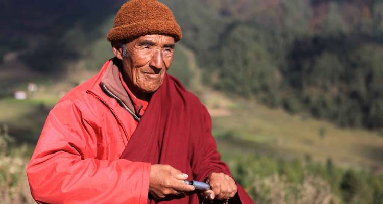Monje anciano en vestimenta tradicional de pie al aire libre.