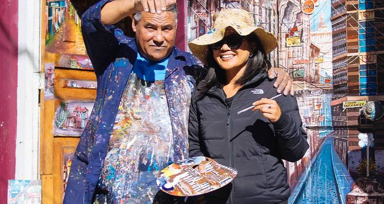 Two people posing with artwork in a colorful street.