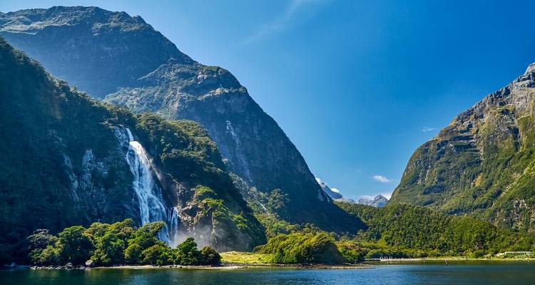 Milford Sound con cascada y montañas bajo un cielo azul.