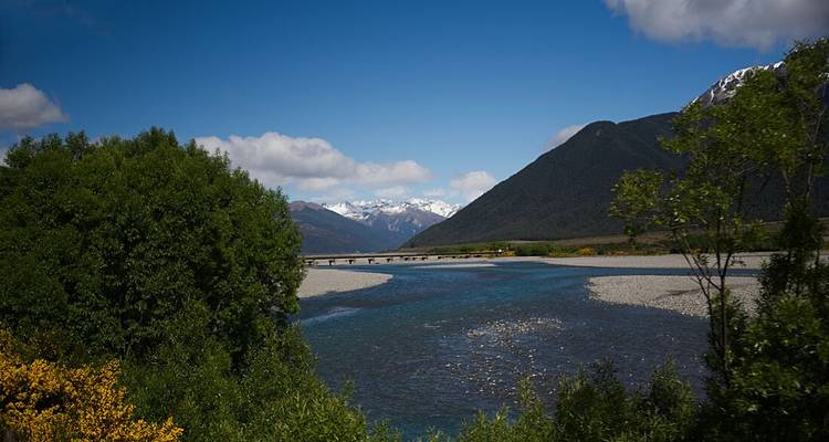 Large fleuve bordé par des montagnes et pont sous un ciel dégagé