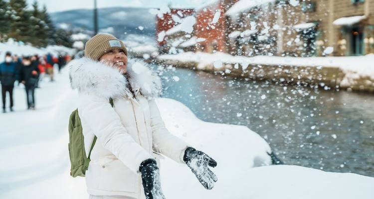Voyageur jetant joyeusement de la neige fraîche au bord du pittoresque canal d'Otaru bordé d'entrepôts historiques.