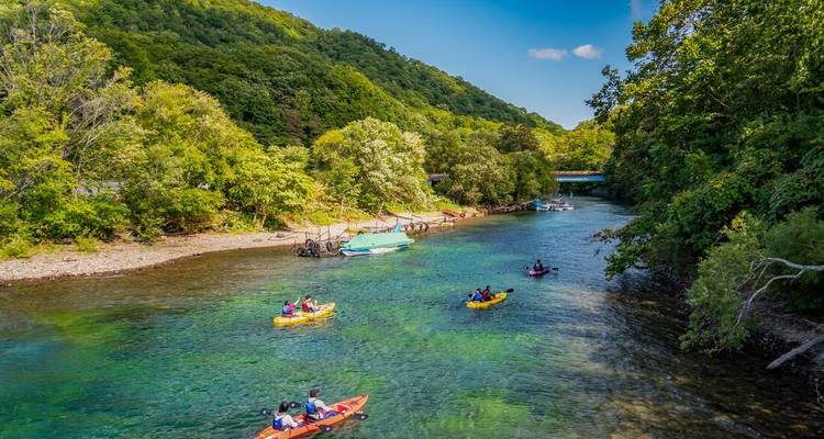 Des kayakistes pagaient le long d'une rivière cristalline entourée de collines boisées d'un vert luxuriant sous un ciel bleu.