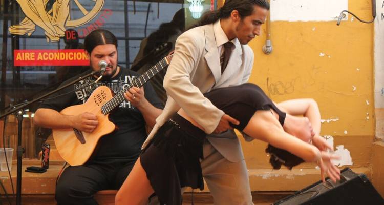 A couple dancing tango with a guitarist in a lively setting.